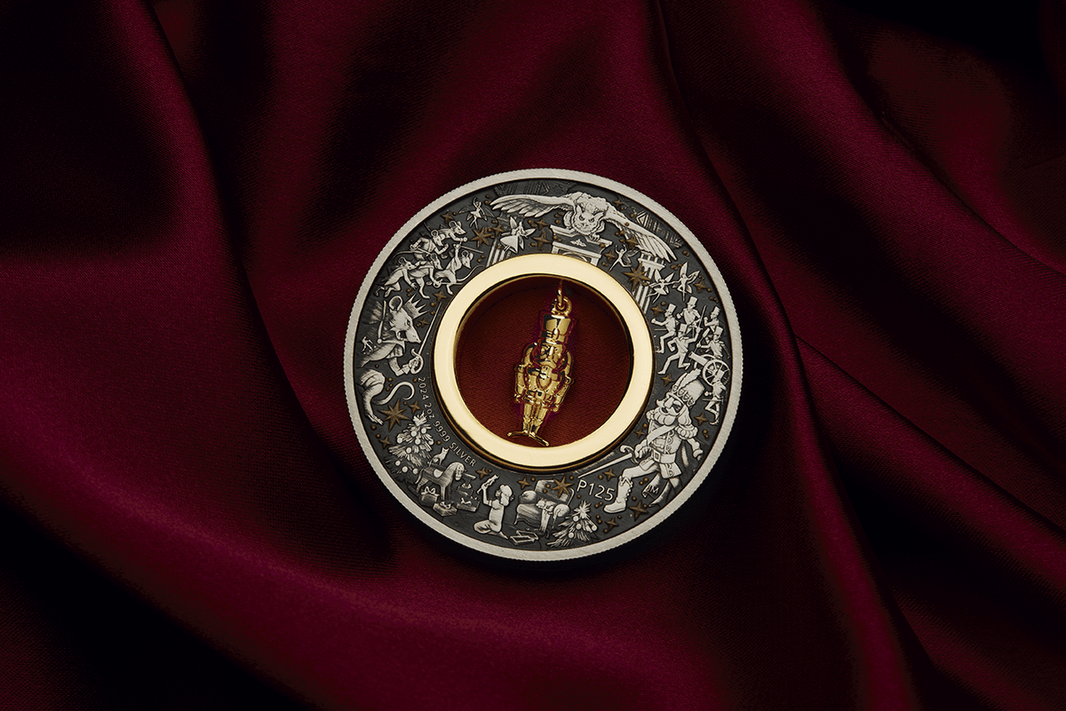 Christmas Nutcracker silver coin displayed on burgundy fabric with its gold-plated figurine hanging upright