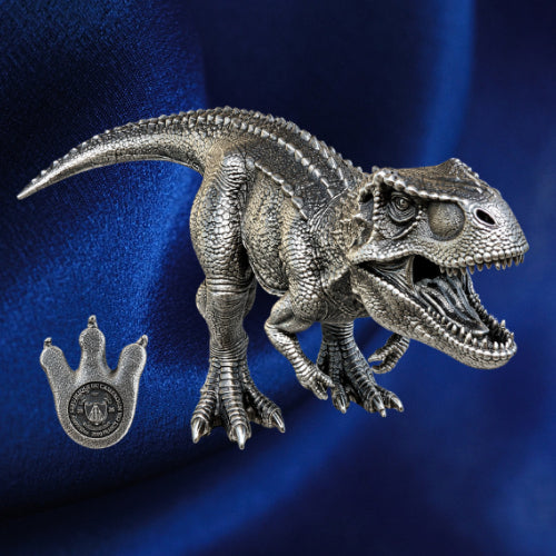 Tyrannosaurus rex three-dimensional silver coin with open jaws beside its footprint-shaped obverse against blue satin.