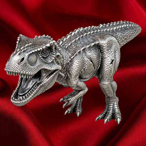 Tyrannosaurus rex three-dimensional silver coin with open jaws, textured scales and clawed feet, viewed from above against red satin.