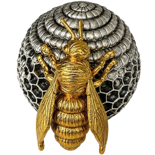 A gold bee figurine positioned in front of a silver beehive-shaped decorative object, set against a dark blue velvet fabric background.