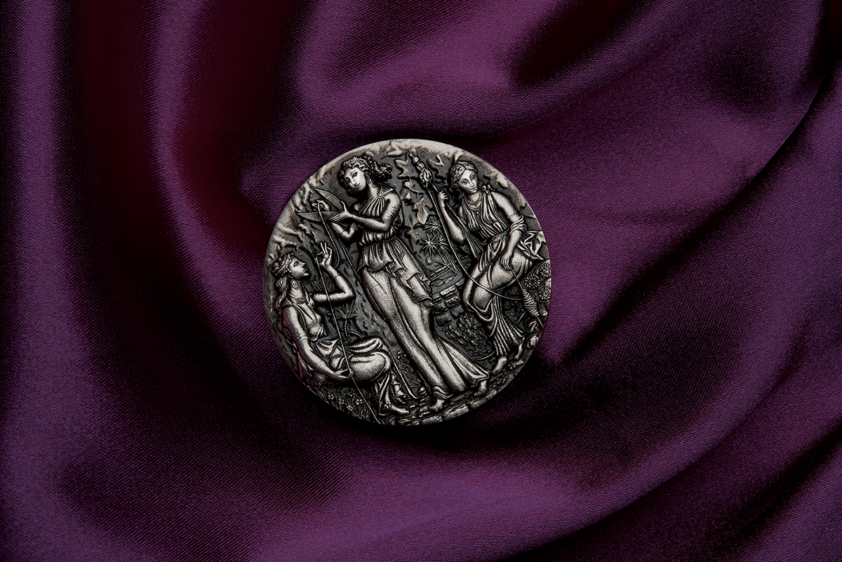 A silver coin with a detailed relief design featuring three ancient goddesses, Clotho, Lachesis, and Atropos, from Greek mythology, within a grove setting. The Coin is in a setting of luxurious purle velvet lying flay giving a birdseye view. The coin is rotated to 11 o'clock.