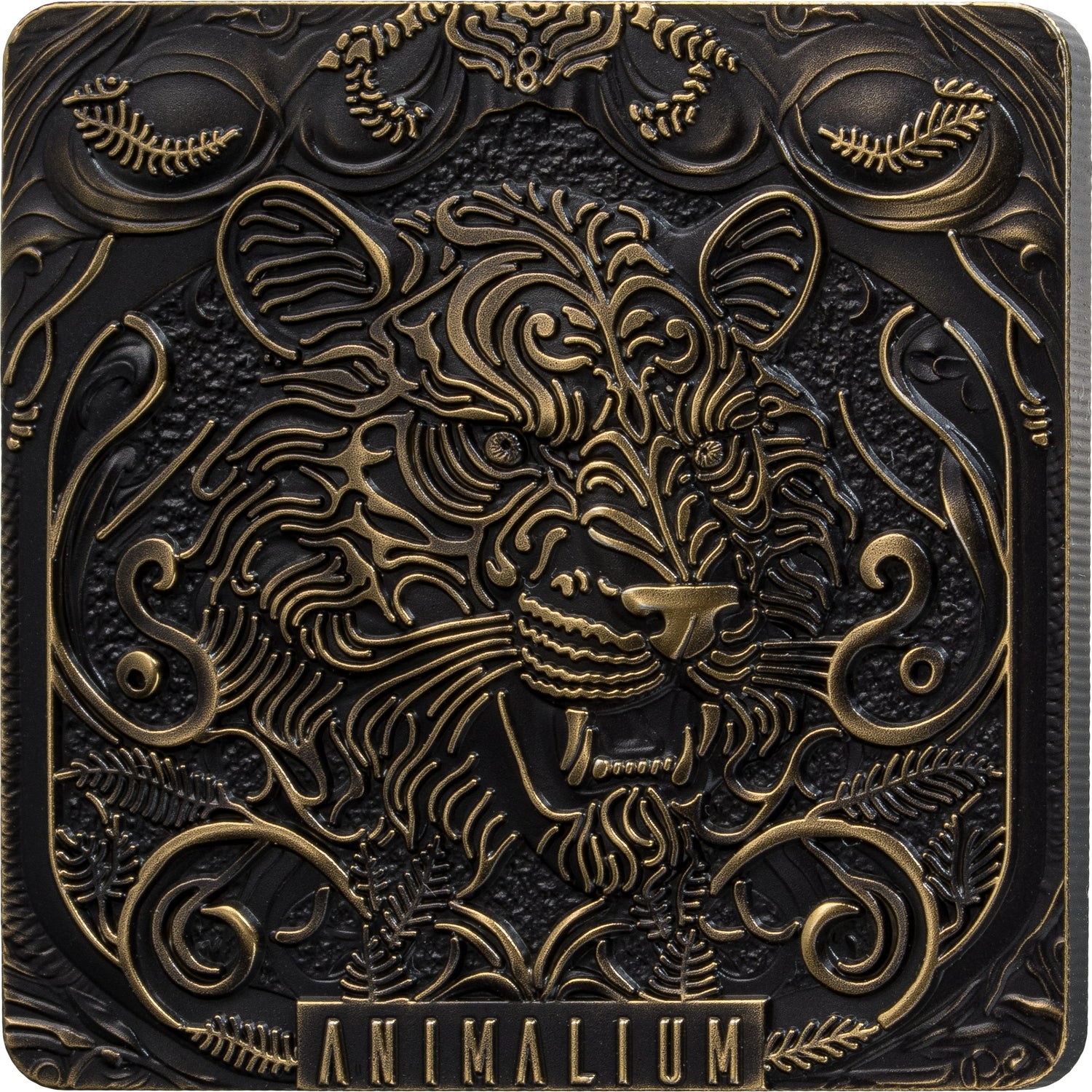 A square decorative plaque or box cover featuring an ornate embossed animal head with swirling floral and scroll motifs, in dark metallic black and antique gold tones. The word 'ANIMALIUM' appears at the bottom.