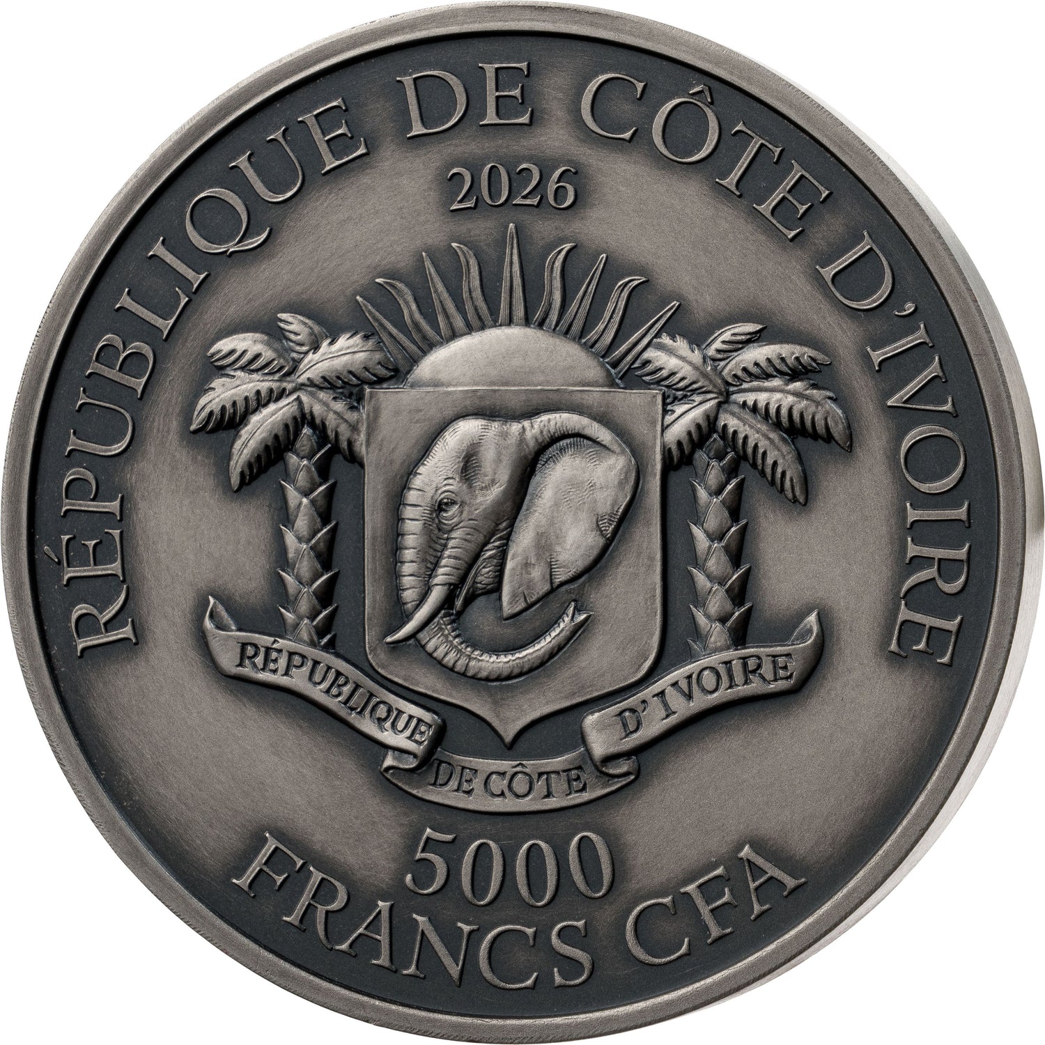 A circular metallic coin or medallion with embossed text reading “RÉPUBLIQUE DE CÒTE D'IVOIRE 2026 5000 FRANCS CFA,” featuring an elephant crest between two palm trees on a plain white background.