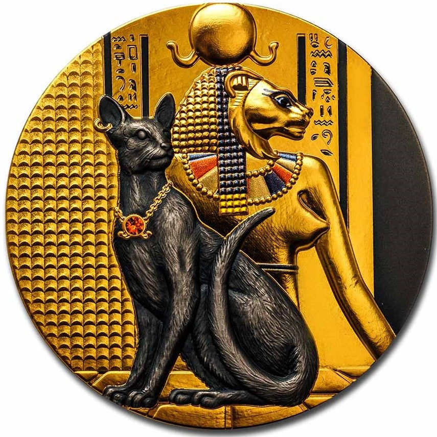 A macro product photograph highlighting the detailed reverse side of the Niue 2023 $5 "Lady Flame" 2-ounce silver coin. Struck in an antiqued finish with ultra-high relief, the coin centers on Sekhmet, the ancient Egyptian warrior goddess portrayed with a powerful lion head. In front of her sits a sleek black cat whose collar is inset with a single, brilliant red Swarovski crystal. The background is richly ornamented with selective gold gilding that illuminates historic Egyptian writing and stylized hierogl