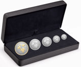 A set of five silver coins with gold plating, including a large coin with a maple leaf design and smaller coins in a case with a molded edge.
