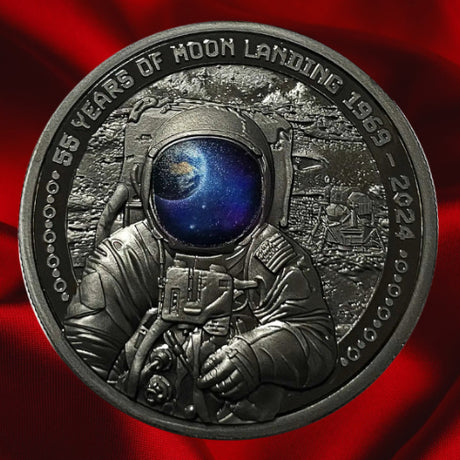 Astronaut on red satin: 2024 Barbados Moon Landing silver black proof coin with Earth reflected in the astronaut’s visor, against red satin.