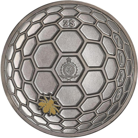 A circular silver-colored medallion or coin featuring a honeycomb pattern, with the number 25 at the top, a central crest, the year 2026 along the right edge, and a small gold bee detail near the bottom left, shown on a plain white background.
