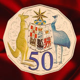 Reverse, warm-lit view: Australia 2012 hyper-metallic 50-cent coin with coloured Coat of Arms and purple 50 denomination under warm lighting.