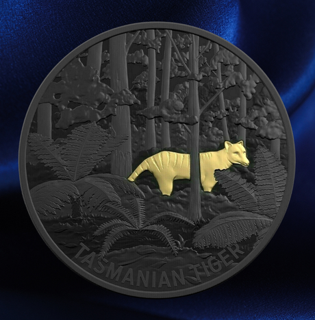 A round commemorative coin featuring a raised gold tasmanian tiger over a dark gray embossed forest background, photographed against a blue satin-like backdrop. The word 'TASMANIAN TIGER' is visible along the bottom edge of the coin.
