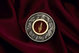 Christmas Nutcracker silver coin displayed on burgundy fabric with its gold-plated figurine hanging upright