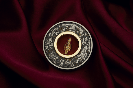 Christmas Nutcracker silver coin displayed on burgundy fabric with its gold-plated figurine hanging upright