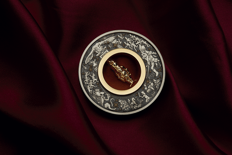 Christmas Nutcracker silver coin on burgundy fabric with its central gold-plated figurine tilted diagonally