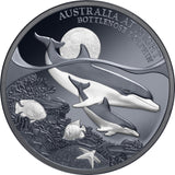 A collectible coin featuring a design of a mother and her calf bottlenose dolphin with a Black Proof finish, accompanied by marine life and the Moonlit black sky in the background.
