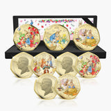 A set of eight gold-plated Peter Rabbit coin medallions displayed in front of their open black presentation box on a white background.