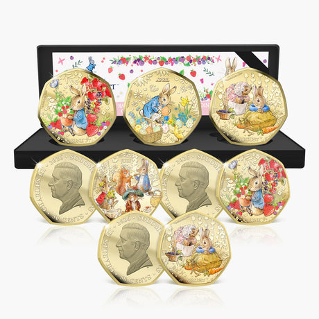 A set of eight gold-plated Peter Rabbit coin medallions displayed in front of their open black presentation box on a white background.