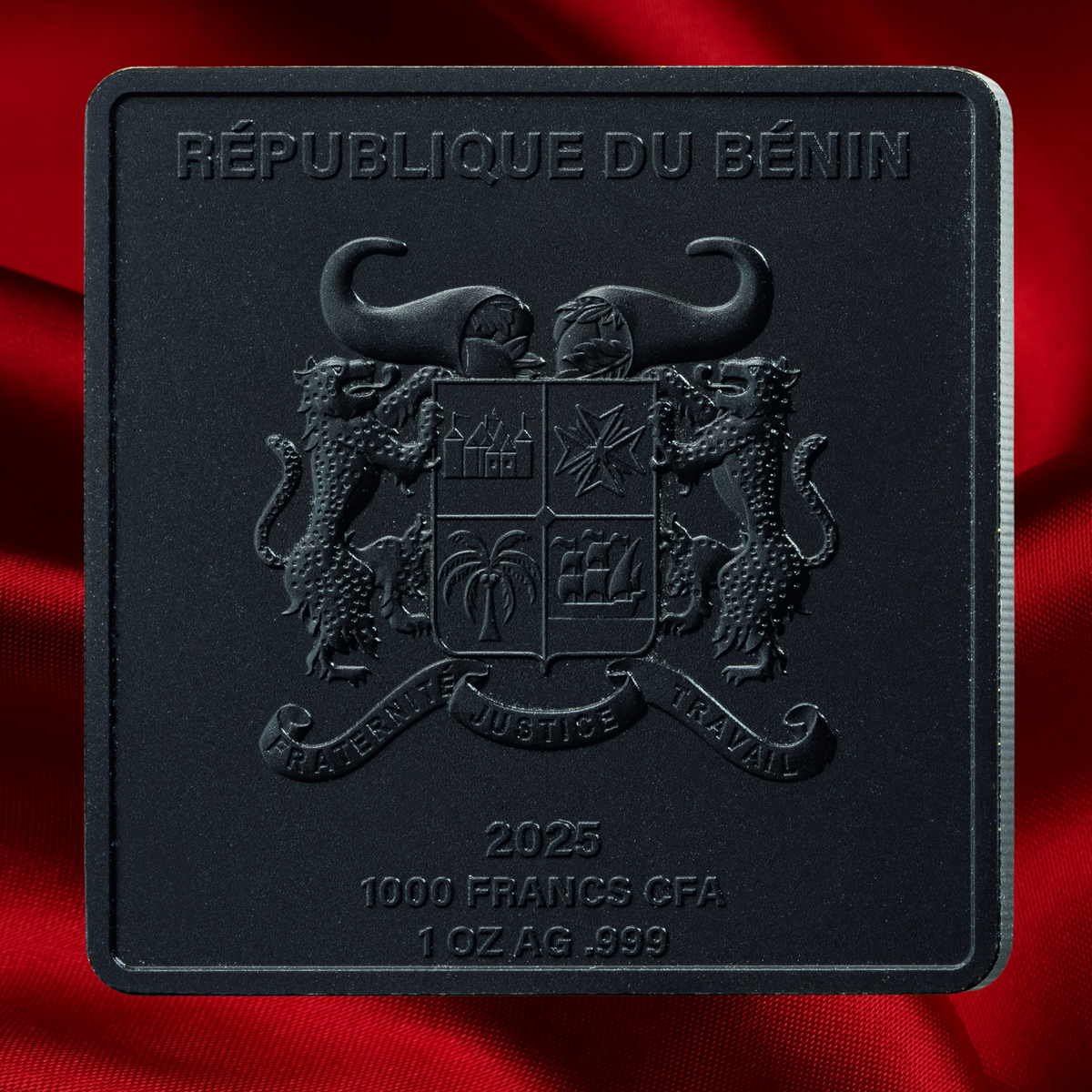 A square black commemorative coin or medallion featuring the Republic of Benin coat of arms and text reading '2025 1000 FRANCS CFA 1 OZ AG .999', shown against a red satin-like fabric background.