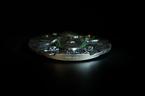 Close-up of a metallic Coin showing a side view of High Relief with engraved text of silver Weight and urity on the rim. The Coin is on a on a dark surface with a dark background.