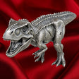 Tyrannosaurus rex three-dimensional silver coin with open jaws, textured scales and clawed feet, viewed from above against red satin.