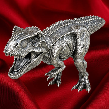 Tyrannosaurus rex three-dimensional silver coin with open jaws, textured scales and clawed feet, viewed from above against red satin.