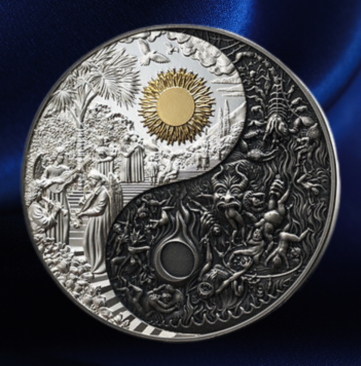 A round silver-toned coin or medallion with an intricate yin-yang design, featuring detailed relief carvings on both halves, a gold sun motif near the top center, and a dark blue satin-like background.