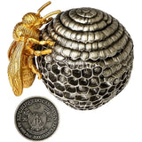 A detailed silver beehive- with a gold bee perched on the left side, displayed on a draped red fabric background the obverse of the coin which is the base of the Beehive is shown below the bee.