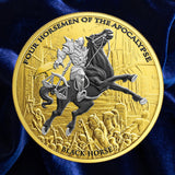 A round gold-toned collectible coin featuring an embossed fantasy scene of a knight on a rearing black horse, with the text 'FOUR HORSEMEN OF THE APOCALYPSE' around the edge and 'BLACK HORSE' at the bottom, displayed on a dark blue satin fabric background.