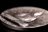 Close-up of a silver coin with detailed  Buddha design on a black background
