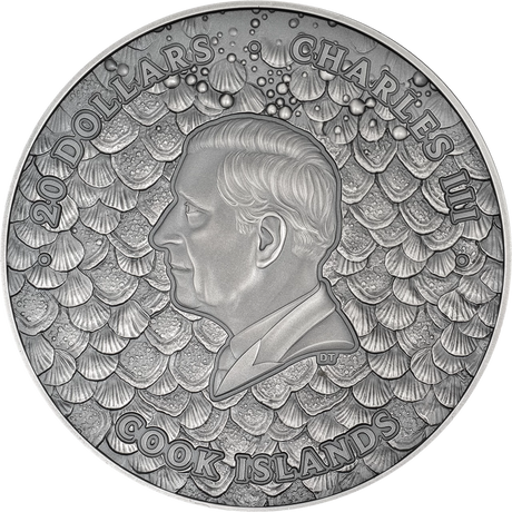 Silver coin with a profile of a person and text '20 Dollars Charles III Cook Islands' on a shell pattern background
