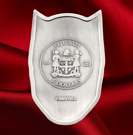 A shield-shaped silver coin featuring the Fiji 2021 5 Dollars emblem, displayed on a rich red satin fabric background. The coin is made of silver with a brushed finish and a raised central seal.