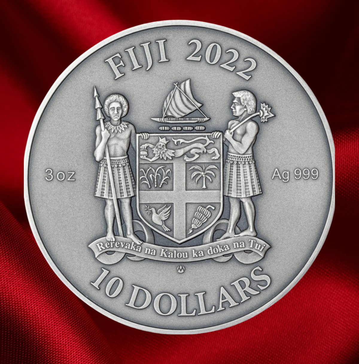 A round silver-colored Fiji 10 Dollars coin featuring the national coat of arms and the year 2022, displayed against a textured red fabric background.