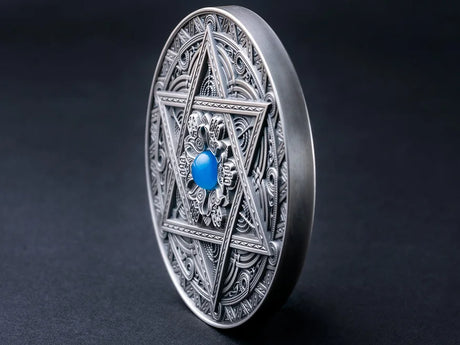 Angled view of a detailed silver coin with a mandala design featuring a central blue gemstone, surrounding by intricate geometric patterns and the star of David and photographed in dramatic lighting standing upright on it's Rim.