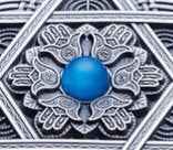 Detail of the reverse side of a silver coin with a mandala design featuring a central blue gemstone, surrounding by intricate geometric patterns and the star of David.