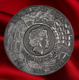 A circular silver-colored commemorative coin of the Republic of Ghana, featuring Queen Elizabeth II and the denomination '10 Cedis' in raised relief, displayed on a draped red fabric background.