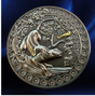 A round metallic medallion or coin featuring an embossed animal and floral design, with a small gold accent near the top right, shown against a dark blue satin-like background.