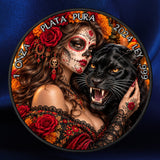 A circular decorative coin or medallion featuring a Day of the Dead-style woman with sugar skull makeup, red roses, black lace clothing, a black panther, and Spanish text reading '1 ONZA PLATA PURA 2024 999' and 'LEY 999'. The plaque is photographed against a dark blue satin-like background.