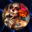 A round commemorative coin featuring a Day of the Dead (Dia de los Muertos) design with a woman in sugar skull makeup, orange and pink roses, and text reading 'PLATA PURA 2024 LEY  .999 1 ONZA'.