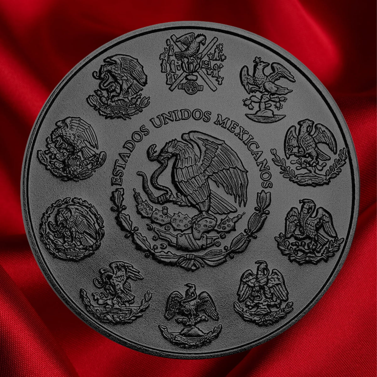 A round black ennobled decorative Mexican 1 oz Silver coin obverse side featuring the Mexican coat of arms, displayed on a rich red satin fabric background.