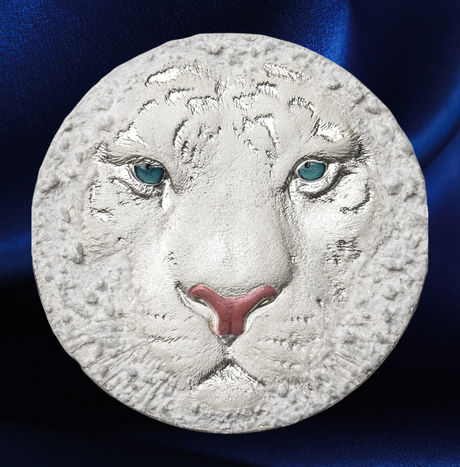 A circular white textured plaque or medallion featuring a sculpted white tiger face with blue eyes and a pink nose, set against a dark blue satin background.