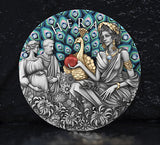 The image on the coin shows Hera with a peacock. Hera is feeding the peacock a pomegranate and the Peacocks feathers are in display with Aquamarine Crystal inserts. To the left is a pregnant woman and a man. The Peacock Body is gilded. His feathers are coloured. Flowers populate the foreground in antiqued silver. 23 sparkling Aquamarine Crystals adorn the feathers. The coin is standing and leaning against a textured charcoal background and Shiny dark ground reflects the coin.