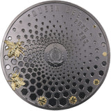 A round dark metallic coin or featuring a honeycomb pattern, embossed text reading 'QUEEN BEE' and '2026 20$', two gold-tone bees on the left, and two small gold bees birthing  from the comb. Background is white.