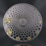 A round dark metallic coin or featuring a honeycomb pattern, embossed text reading 'QUEEN BEE' and '2026 20$', two gold-tone bees on the left, and two small gold bees birthing  from the comb. Coin is photographed on a dark  greyreflective background.