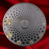 A round dark metallic coin or featuring a honeycomb pattern, embossed text reading 'QUEEN BEE' and '2026 20$', two gold-tone bees on the left, and two small gold bees birthing  from the comb. Background is white.