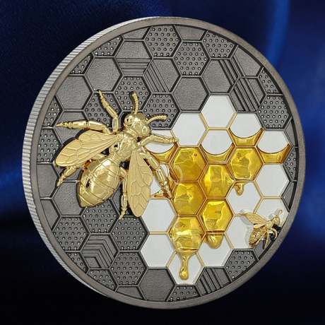 A round collectible coin featuring a detailed gold bee and honeycomb design on a textured silver background, set against a dark blue backdrop.