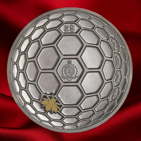 A round silver-colored commemorative coin with a honeycomb pattern, featuring a gold spider emblem near the bottom left and the text '2025' along the right edge, set against a draped red fabric background.
