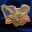A detailed eagle emblem with outstretched wings over an American flag motif, finished in a metallic gold tone, set against a dark blue satin fabric background.