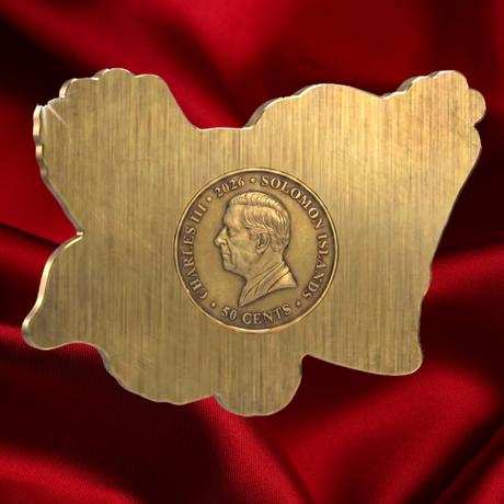 A gold-colored commemorative coin or medallion shaped like the map of Solomon Islands, featuring a profile portrait of Charles III in the center, displayed on a draped red satin fabric background.