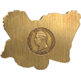 A gold-colored metal plaque shaped like the map of Solomon Islands, featuring a central circular relief of a profile portrait and the text 'CHARLES III • 2026 • SOLOMON ISLANDS • 50 CENTS'.