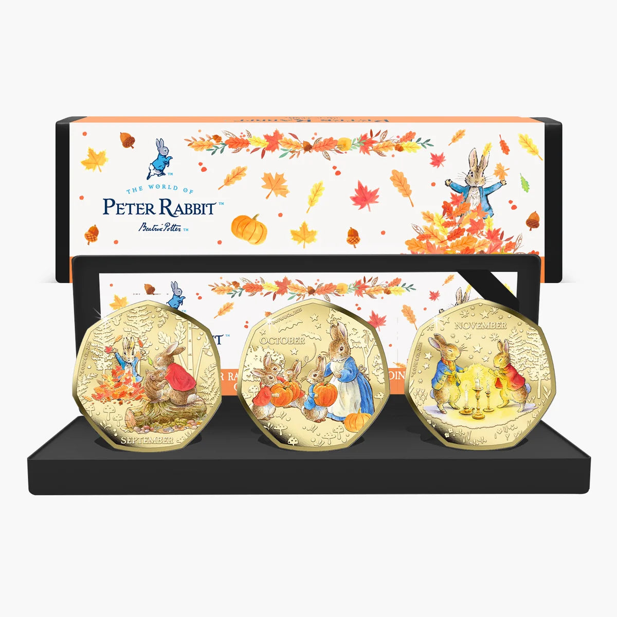 Peter Rabbit Tales of Autumn three coloured coins in an open presentation case with autumn-themed packaging behind.