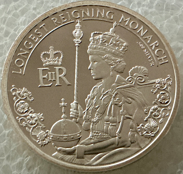 Silver coin featuring a monarch with decorative elements and text on a textured background
