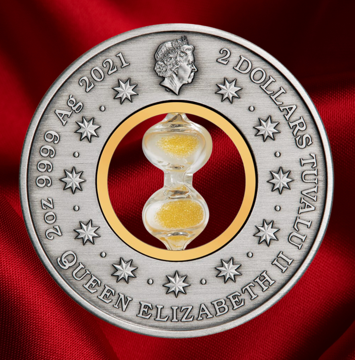 A round silver commemorative coin featuring a central clear glass hourglass filled with gold sand, set against a red fabric background. The coin is inscribed with '2 DOLLARS TUVALU II QUEEN ELIZABETH II 9999 Ag 2021' and features a profile of Queen Elizabeth at the top.